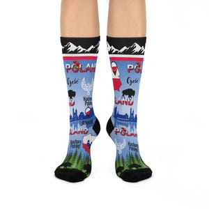 May include: A pair of socks with a Polish theme. The socks feature a light blue background with illustrations of mountains, a map of Poland, a bison, and the Polish flag. The word "Poland" is printed on the socks, along with other Polish words.