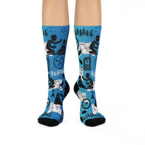 Pode incluir: Um par de meias azuis com um padrão de silhuetas pretas de pessoas com bússolas, mapas e outros equipamentos de aventura ao ar livre. As meias são feitas de um material macio e confortável e são perfeitas para o uso diário.