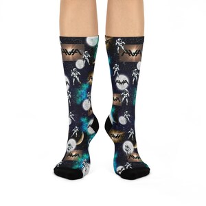 May include: A pair of crew socks with a space-themed design. The socks feature a dark blue background with white astronauts, planets, and the text "AVA". The socks have black heels and toes.