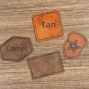 May include: Four leather patches in shades of brown and tan are arranged on a wooden surface. One patch is a rectangle, another is a square with "Tan" printed on it, a third is a shield shape with a star design, and the last is a hexagon with "Camel" printed on it.