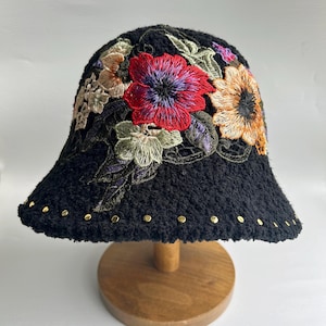 May include: A black bucket hat with embroidered flowers in shades of red, yellow, green, and purple. The hat has gold studs around the brim.