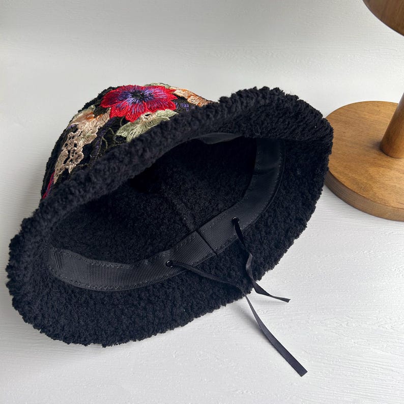 Puede incluir: Sombrero cubo negro con forro de borreguito suave y un dise&ntilde;o de bordado floral en tonos rojos, rosas, verdes y blancos.