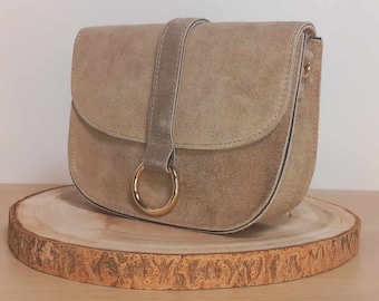 Sac en cuir, daim ou suède, "Andromeda" de couleur beige et avec sangle assortie. Finitions métalliques en acier brillant.