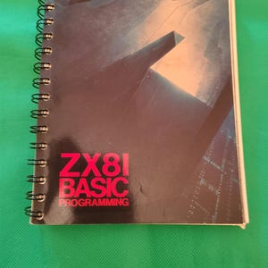 May include: A spiral-bound notebook with a dark cover featuring the text "ZX81 BASIC PROGRAMMING" in red. The cover has a futuristic design with a dark colour scheme and the Sinclair logo at the top.