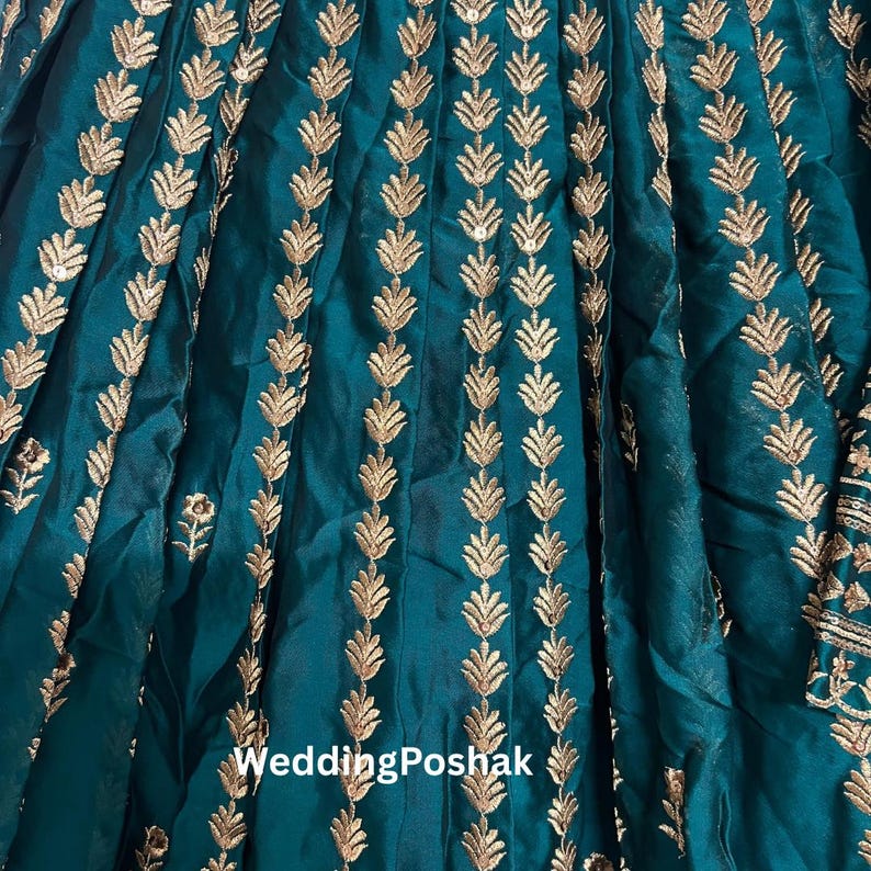 K&ouml;nnte beinhalten: T&uuml;rkisfarbener Stoff mit goldener Blattstickerei. Der Stoff ist gerafft und flie&szlig;end, mit dem Text "Wedding Poshak" unten. Die goldene Stickerei ist detailliert und verleiht dem Textil Eleganz.
