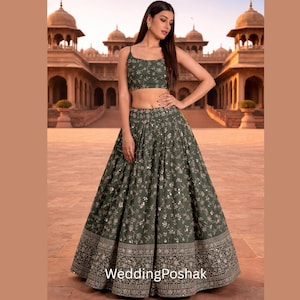 May include: An olive green two-piece outfit with floral embroidery and sequin accents. The set includes a crop top and a flowing skirt. The skirt features a detailed border design. The text "WeddingPoshak" is visible at the bottom.