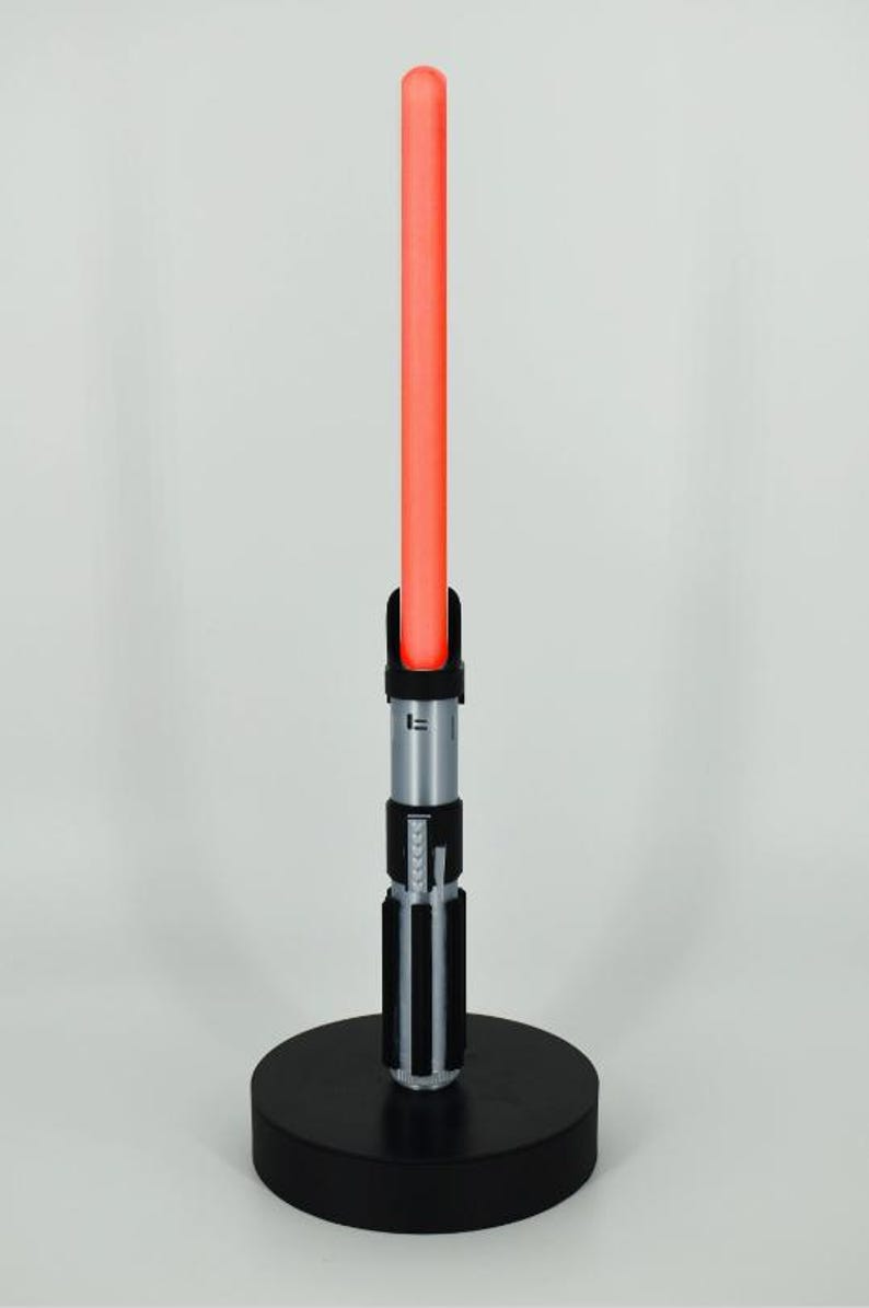 Op de afbeelding: Een zwart lightsaber met een rode blade op een zwarte basis. De lightsaber heeft een zilveren handvat met zwarte accenten.