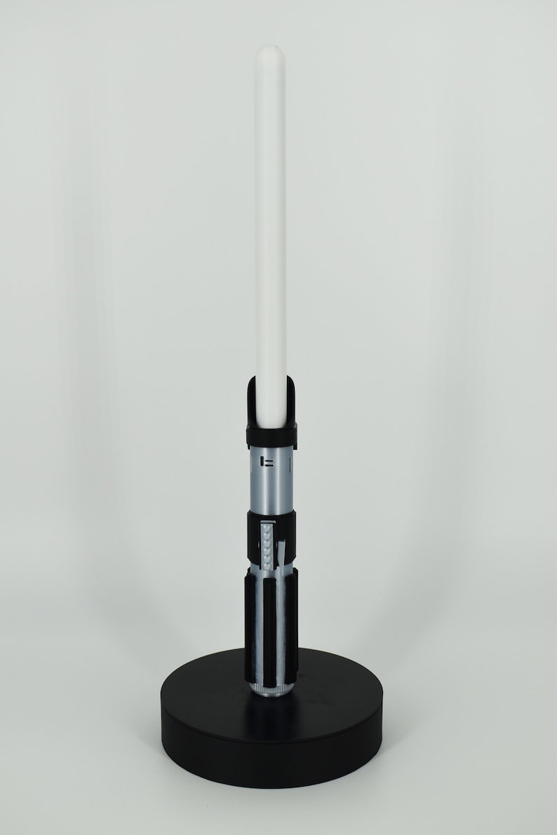 Op de afbeelding: Een zwarte lightsaber-standaard met een witte lightsaber-blade. De lightsaber is zilver met zwarte accenten.