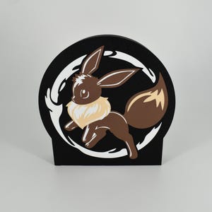 Puede incluir: Una pieza decorativa negra, semicircular, con un personaje de dibujos animados marrón con un collarín color crema y una cola esponjosa. El personaje está sobre un diseño blanco arremolinado sobre un fondo negro. Es una decoración de pie.