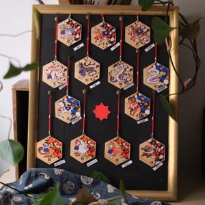 Peut inclure: Un ensemble de 12 ornements hexagonaux en bois représentant les animaux du zodiaque chinois. Chaque ornement est peint avec une illustration colorée de l'animal et des caractères chinois. Les ornements sont affichés sur un fond noir avec une ficelle rouge.