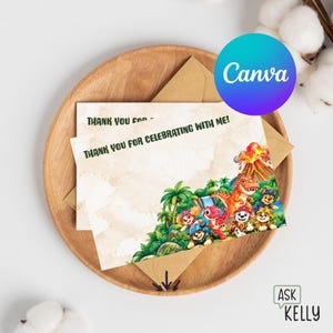 Op de afbeelding: Een rechthoekige bedankkaart met een kleurrijke illustratie van tekenfilmhonden en een dinosaurus in een jungleomgeving met een vulkaan. De tekst op de kaart luidt: "THANK YOU FOR CELEBRATING WITH ME!". De kaart ligt op een bruine envelop.