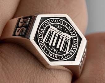 Może przedstawiać: Srebrny pierścień z czarną sześciokątną pieczęcią przedstawiającą logo Virginia Commonwealth University i tekst "Virginia Commonwealth University - MCV - RPI - 1838".