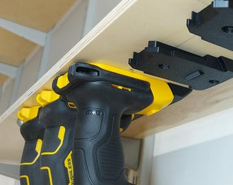 May include: Two black and yellow cordless drills with the word "BRUSHLESS" printed on the side, hanging on a wooden shelf with black plastic mounts.