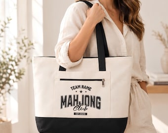 May include: A cream-colored canvas tote bag with black handles and a black base. The front features a zippered pocket with black text that reads TEAM NAME MAHJONG Club EST.2026, accented by two small stars above the word MAHJONG.