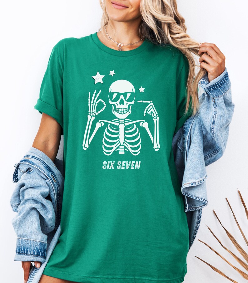 以下が含まれることがあります： サングラスをかけた白い骸骨のグラフィックが特徴の緑色のTシャツ。骸骨の下には「SIX SEVEN」の文字。骸骨の頭の上には2つの星があります。