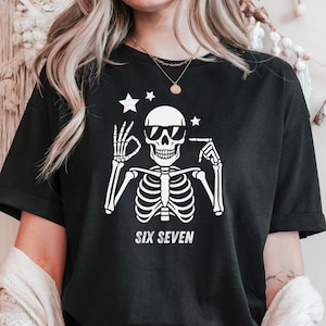 以下が含まれることがあります： サングラスをかけた白い骸骨のグラフィックが特徴の黒いTシャツ。骸骨の下には「SIX SEVEN」の文字がプリントされています。カジュアルなユニセックススタイルです。