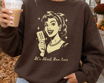 May include: A dark chocolate brown crewneck sweatshirt featuring a cream-colored graphic of a retro-style person holding a popsicle. The design includes star accents and the text It's About Bam time printed in a script font below the illustration.