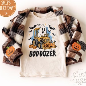 May include: A cream-colored long-sleeved shirt with a Halloween-themed graphic of a ghost driving a bulldozer, with the text "BOO-DOZER". The shirt is paired with a brown and cream plaid jacket with pumpkin patches.