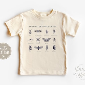 May include: A cream-colored t-shirt with the text "Future Entomologist" printed on the front. The shirt features a graphic of various insects, including a dragonfly, cricket, bee, and beetle.
