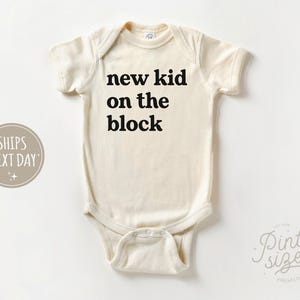 May include: A white baby onesie with black text that reads "new kid on the block".