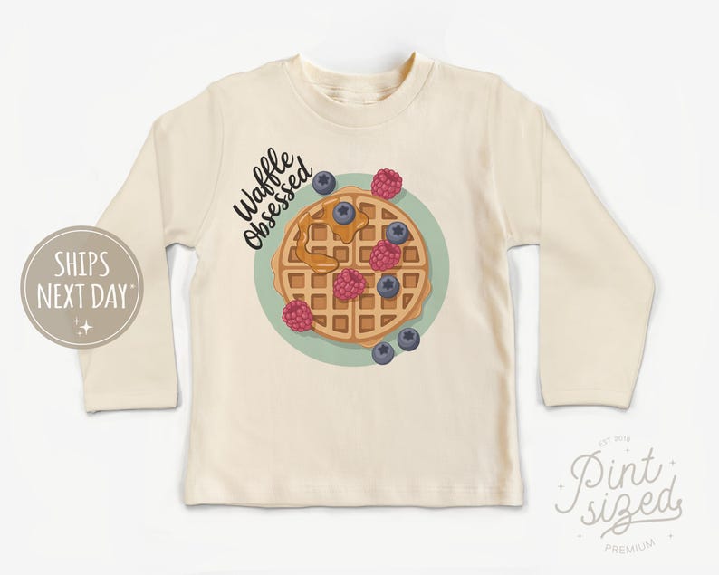 Peut inclure: T-shirt cr&egrave;me &agrave; manches longues avec un motif de gaufre, des myrtilles et des framboises. Le texte "Waffle Obsessed" est au-dessus du motif de la gaufre. Le t-shirt a un col rond et des manches longues.