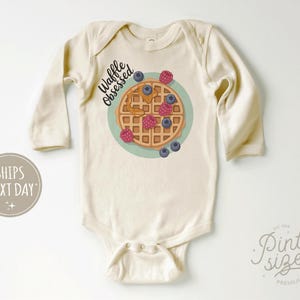 Peut inclure: Body de b&eacute;b&eacute; cr&egrave;me &agrave; manches longues. Le devant pr&eacute;sente un dessin de gaufre avec des myrtilles, des framboises et du sirop, ainsi que le texte "Waffle Obsessed". Une tenue mignonne et confortable pour b&eacute;b&eacute;s.