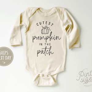May include: A white long-sleeve bodysuit with the text "Cutest pumpkin in the patch" in black lettering. A small pumpkin graphic is above the text.