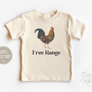 May include: A cream colored short-sleeved t-shirt with a brown and black rooster illustration and the text "Free Range" printed on the front.