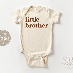 May include: A white baby onesie with the words "little brother" printed in brown on the front.