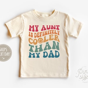 May include: A cream colored short-sleeved t-shirt with the text "My Aunt is Definitely Cooler Than My Dad" in rainbow colors.