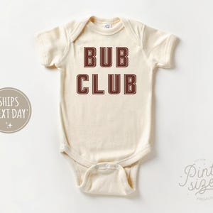 May include: A cream-colored baby onesie with the text "Bub Club" in brown letters.