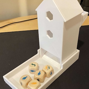 Puede incluir: Torre de dados de madera blanca con una bandeja y seis dados de madera con diferentes símbolos. Los dados tienen imágenes de peces, trigo y un gusano.