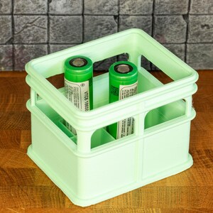 May include: A light green plastic crate with two green cylindrical batteries inside. The batteries have labels with the text "VTC6 18650".