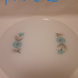May include: A white plate with a floral design. The plate features two clusters of blue flowers with brown and green leaves. The text "plate 2" is written in blue at the top of the image.