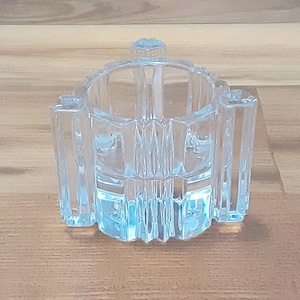 May include: A clear glass candle holder with a geometric design. The holder has a round base and a cylindrical shape. The glass is clear and has a slight blue tint.