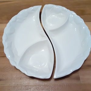May include: White ceramic serving dish with three sections. The dish is divided into three sections, two of which are crescent-shaped and one of which is a smaller, round section.