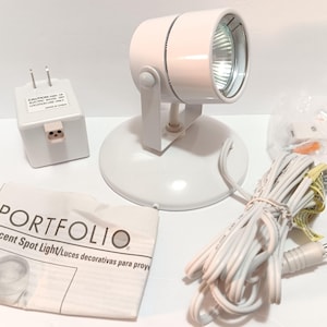 May include: White accent spot light with a round base and adjustable head. Includes a power adapter, cord, and a Portfolio instruction sheet. The light is designed for accent lighting.