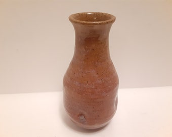 May include: A small, brown ceramic vase with a speckled glaze. The vase has a narrow neck and a rounded body.
