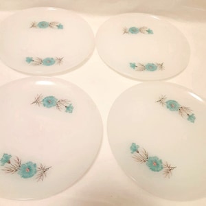 May include: Four white oval plates with a floral design. Each plate features a cluster of turquoise flowers with gray and brown leaves. The plates are arranged in a square formation.