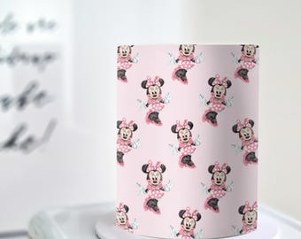 May include: A pink cake with a Minnie Mouse print. The cake is decorated with a repeating pattern of Minnie Mouse in her signature red dress and white polka dots.
