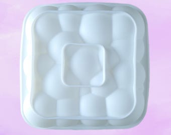 May include: White silicone mould with a square shape and a raised design of multiple rounded circles. The mould is designed for making multiple round cakes or desserts.