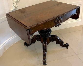May include: A dark wood drop leaf table with intricate carvings on the legs and a single drawer. The table has a rounded edge and sits on four legs.