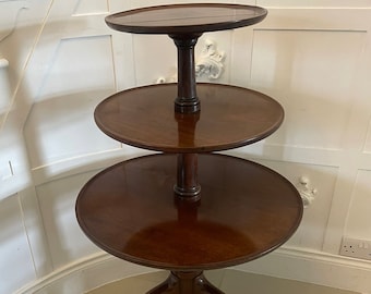 May include: A three-tiered mahogany serving table with a round top and three cabriole legs. The table is made of dark wood and has a polished finish.