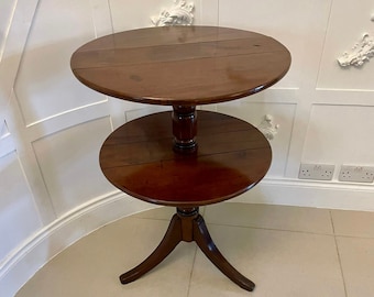 May include: A two-tiered round wooden table with a turned pedestal base and a dark brown finish. The table has a simple design and is perfect for a small space.