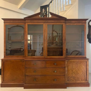 May include: A large, antique wooden bookcase with glass doors and drawers. The bookcase has a dark wood finish and is decorated with intricate carvings. It is a beautiful piece of furniture that would be perfect for a library or study.