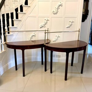 May include: Two mahogany half-round tables with brass accents and a connecting brass rail. The tables are in a room with white walls and a white staircase in the background.