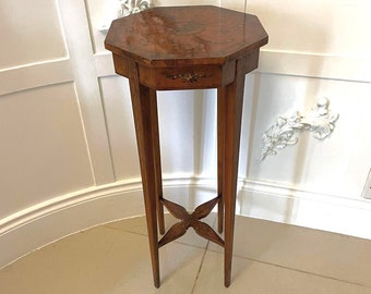 May include: A small, octagonal, wooden table with a single drawer and intricate marquetry inlay. The table has four legs that are connected by a cross-shaped stretcher.