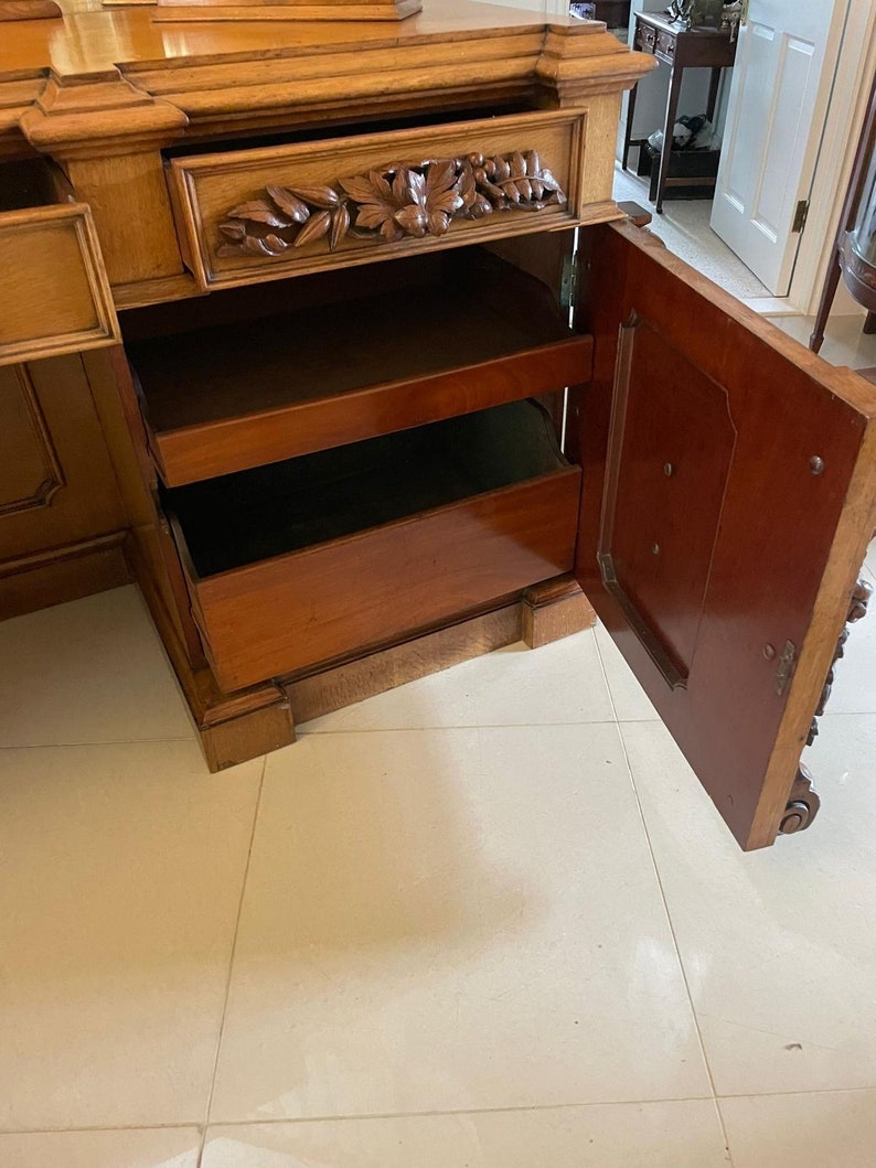 May include: A wooden cabinet with a carved drawer and open shelves. The cabinet has a dark wood finish and is decorated with intricate carvings. The cabinet is open and the shelves are empty.