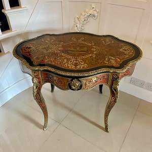 Puede incluir: Una peque&ntilde;a mesa ovalada antigua con incrustaciones de marqueter&iacute;a intrincada en la parte superior. La mesa tiene una base de madera oscura con detalles de lat&oacute;n ornamentados y patas curvas.