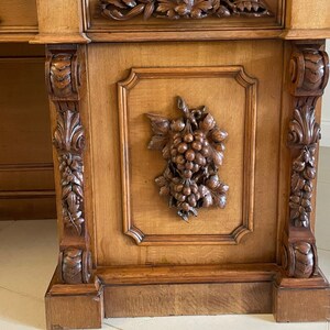May include: A large, antique wooden cabinet with intricate carvings of grapes and leaves. The cabinet has a dark brown finish and is decorated with ornate details.